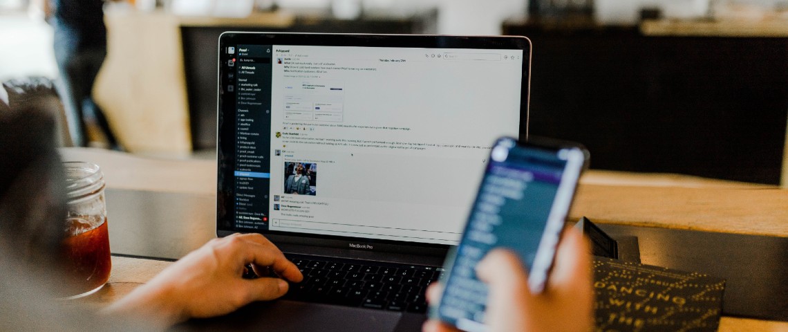 Télétravail : la multiplication des outils numériques angoisse certains salariés Personne en train de regarder son téléphone portable et Slack sur son ordinateur en simultané