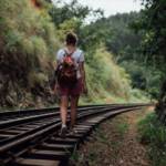 Une jeune femme marche sur des rails de trains entourés de verdure