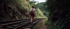Une jeune femme marche sur des rails de trains entourés de verdure