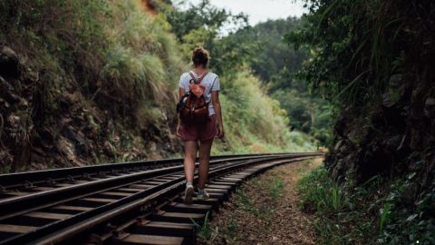Une jeune femme marche sur des rails de trains entourés de verdure