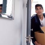 Un jeune homme avec un carton de déménagement qui rentre dans une maison
