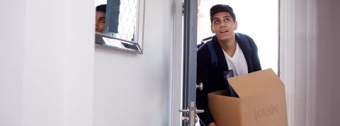 Génération boomerang : les jeunes retournent chez leurs parents Un jeune homme avec un carton de déménagement qui rentre dans une maison