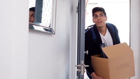 Un jeune homme avec un carton de déménagement qui rentre dans une maison