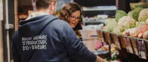 Une femme en train d'acheter des fruits et légumes chez Biocoop se faisant aider par un vendeur