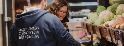 Comment fonctionne le modèle Biocoop ? Une femme en train d'acheter des fruits et légumes chez Biocoop se faisant aider par un vendeur