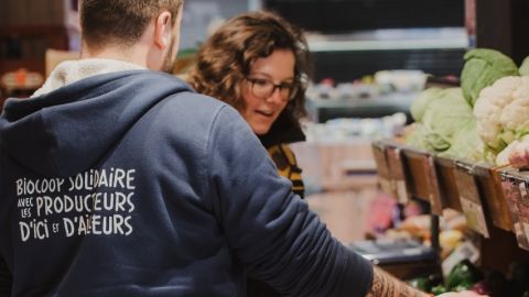 Une femme en train d'acheter des fruits et légumes chez Biocoop se faisant aider par un vendeur