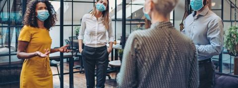 Quel est l'état d'esprit des dirigeants face à la crise Une femme en réunion avec ses employés, portant un masque, en entreprise