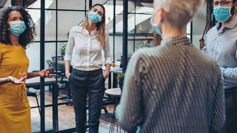 Quel est l'état d'esprit des dirigeants face à la crise Une femme en réunion avec ses employés, portant un masque, en entreprise