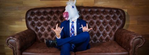 Homme avec masque de licorne en costume cravate sur un canapé.