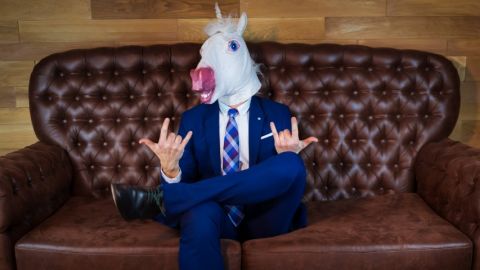 Homme avec masque de licorne en costume cravate sur un canapé.