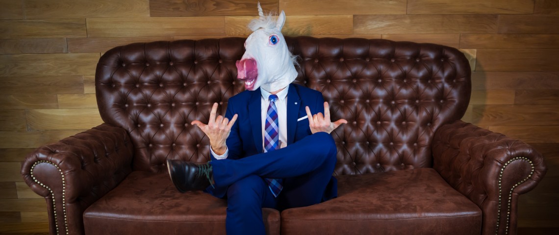 Homme avec masque de licorne en costume cravate sur un canapé.