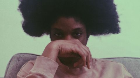 Un jeune homme noir avec une coupe afro et sa main devant le visage