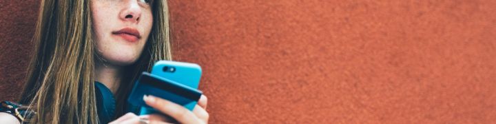 Une adolescente avec un smartphone adossé à un mur