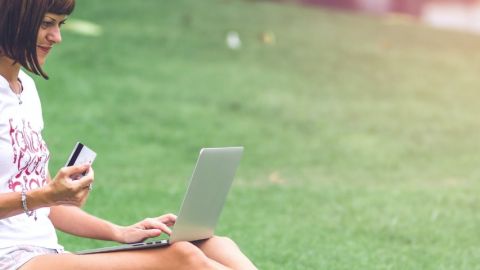 Amazon lance une plateforme écologique Une femme faisant ses courses sur son ordinateur portable, assise dans l'herbe