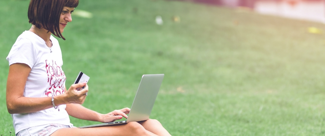 Amazon lance une plateforme écologique Une femme faisant ses courses sur son ordinateur portable, assise dans l'herbe