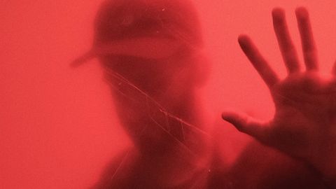 Un homme derrière une parois rouge.