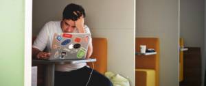 jeune homme devant un ordinateur l'air desespéré, seul dans une salle.
