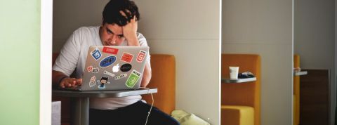 jeune homme devant un ordinateur l'air desespéré, seul dans une salle.