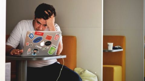 jeune homme devant un ordinateur l'air desespéré, seul dans une salle.