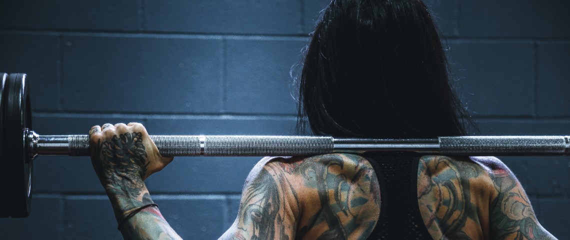 Anti-fragile : muscu is the new yoga Une femme tatouée de dos porte un haltère