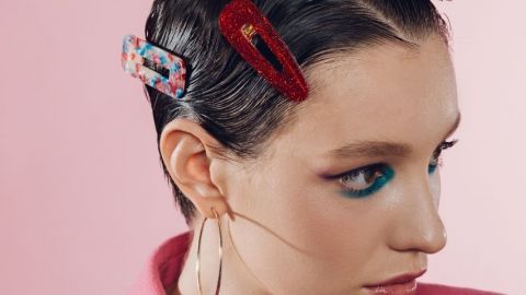 Une femme avec des barrettes colorées dans les cheveux sur fond rose