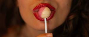 Gros plan sur la bouche du femme avec du rouge à lèvres qui mange une sucette