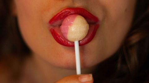 Gros plan sur la bouche du femme avec du rouge à lèvres qui mange une sucette