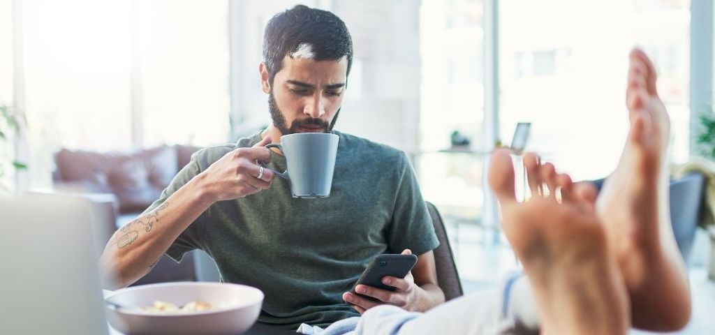 Réalistes, positifs… quels messages adresser en temps de Covid ? Homme tient une tasse et regarde son téléphone