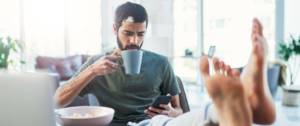 Homme tient une tasse et regarde son téléphone