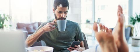 Réalistes, positifs… quels messages adresser en temps de Covid ? Homme tient une tasse et regarde son téléphone