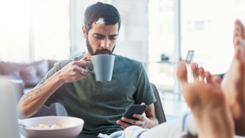 Homme tient une tasse et regarde son téléphone