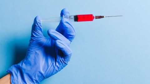 Une main gantée tenant une seringue remplie d'un liquide rouge