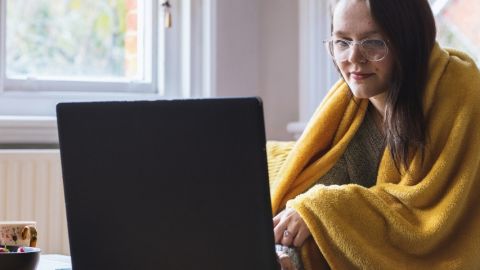 Une jeune femme, un plaid enroulé autour de ses épaules, sur son ordinateur