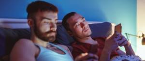 Un couple dans un lit consulte smartphone