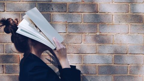 Une femme se cache le visage avec un livre