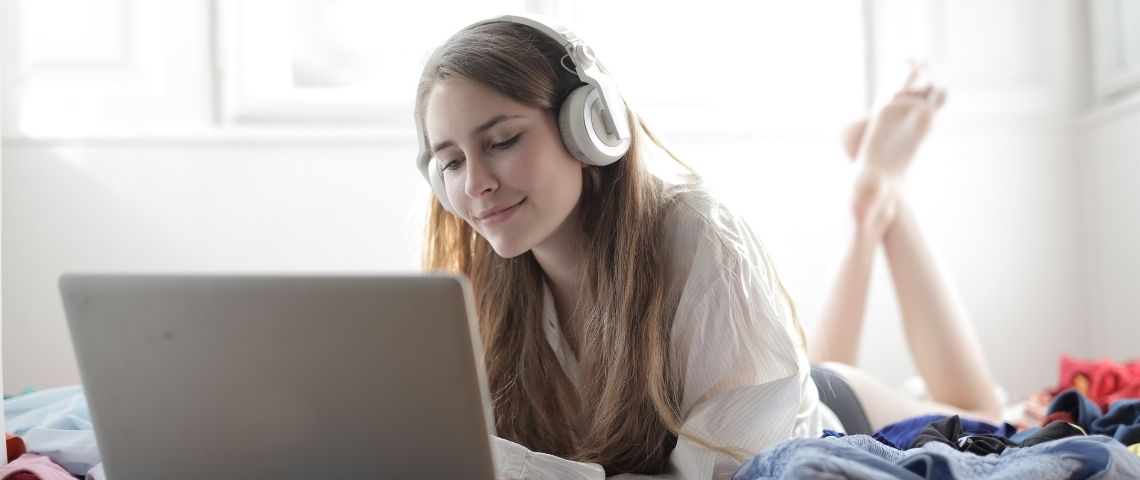 Le média Slate France s’associe à l’adtech Audion pour la monétisation exclusive des contenus audio du groupe Jeune fille allongée sur son lit, devant un ordinateur avec un casque sur les oreilles