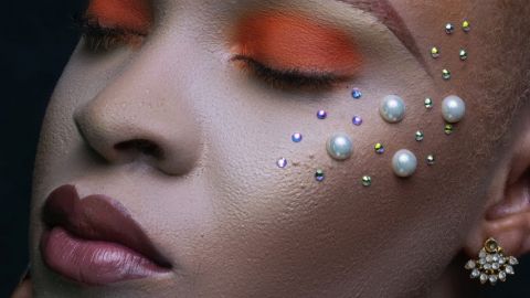 Une femme métisse, les yeux fermés, les paupières fardées d'orange et des perles posées sur les joues