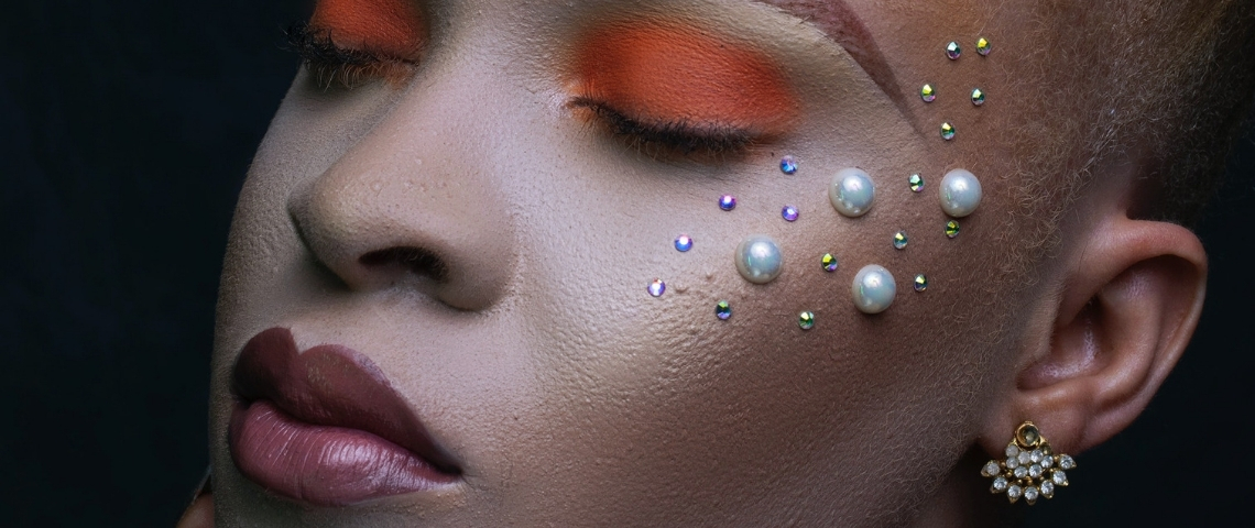 Quel a été l'impact de 2020 sur la beauté ? Une femme métisse, les yeux fermés, les paupières fardées d'orange et des perles posées sur les joues