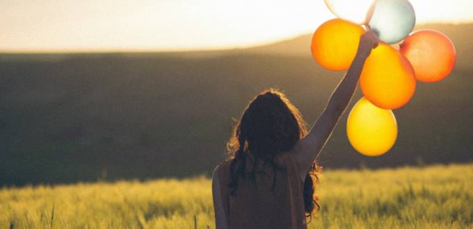 Une femme tient 5 ballons dans la nature