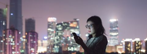 Influenceur et téléachat, super appli... Pour comprendre le web de demain, il faut regarder la Chine Une jeune femme regarde son smartphone dans un centre ville chinois entourée de building