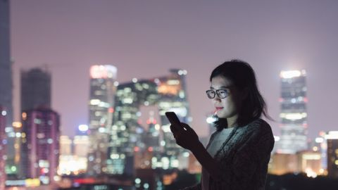 Une jeune femme regarde son smartphone dans un centre ville chinois entourée de building