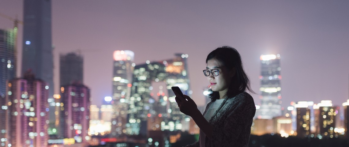 Influenceur et téléachat, super appli... Pour comprendre le web de demain, il faut regarder la Chine Une jeune femme regarde son smartphone dans un centre ville chinois entourée de building