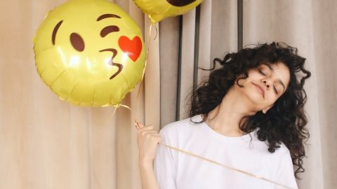 Comment se remonter le moral pendant le confinement ? Une femme brune tenant dans la main un ballon en forme de smiley qui envoie un bisou coeur