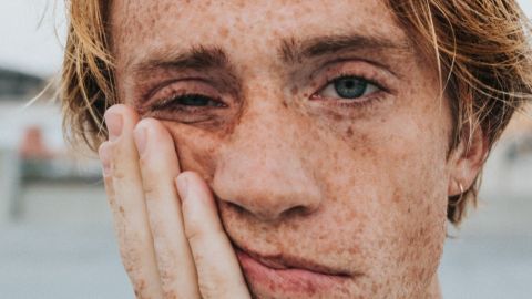 Gros plan sur la tête d'un jeune homme l'air ennuyé, se colle la main sur la joue