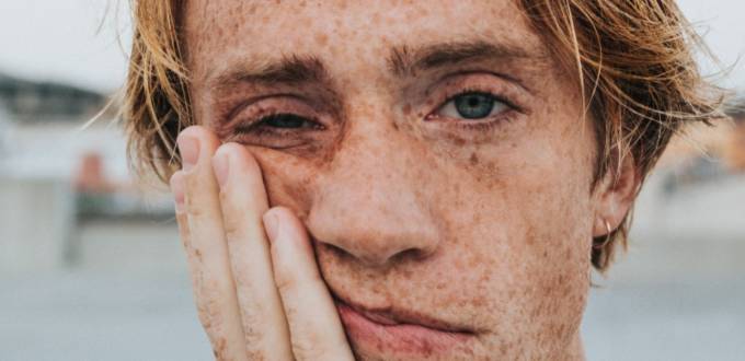 Gros plan sur la tête d'un jeune homme l'air ennuyé, se colle la main sur la joue