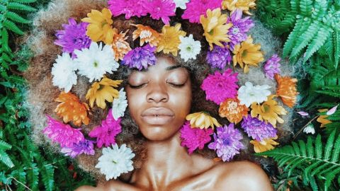 Une femme noire posant sur des feuilles, les cheveux remplis de fleurs