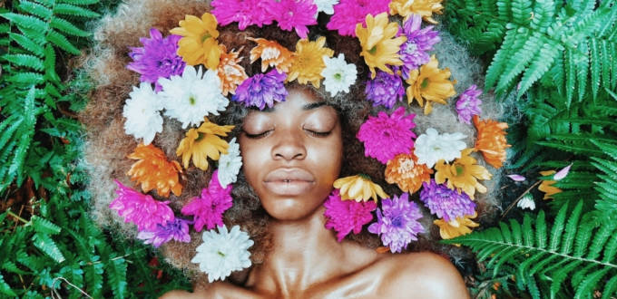 Une femme noire posant sur des feuilles, les cheveux remplis de fleurs
