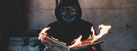 Comment l'intelligence économique peut sauver les entreprises des théories complotistes ? Un homme masqué en train de lire un journal en feu