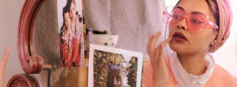Qui sont les pros de la mode vintage ? Une femme en train de se maquiller devant un miroir, portant un turban et des lunettes roses