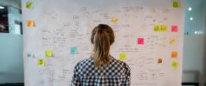 Une femme devant un tableau recouvert de post-it et de notes